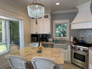 A kitchen with white cabinets, a chandelier, a dining table with wicker chairs, and a Wolf oven. - Daybreak Cottage Walk to Beach, Town and Yacht Club sit on the Front Porch  (Harbor Springs)