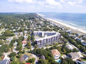 An aerial view of a coastal residential area with a large hotel featuring a central courtyard and multiple balconies, surrounded by single-family homes and a beach. - Gorgeous, Minutes to Beach, Updated Retreat 414 (Pawleys Island)