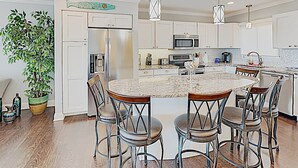 A modern kitchen with a central island, bar stools, stainless steel appliances, and a potted plant. - Gorgeous, Minutes to Beach, Updated Retreat 414 (Pawleys Island)