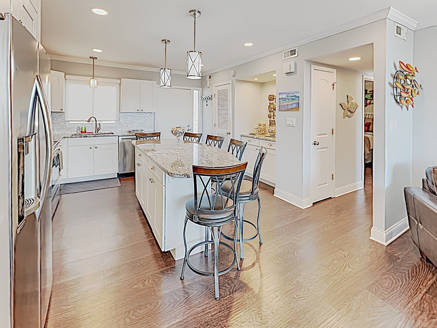 A modern kitchen with white cabinets, a marble island, and pendant lighting.