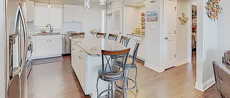 A modern kitchen with white cabinets, a marble island, and pendant lighting.