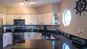 A modern kitchen with white cabinets, stainless steel appliances, a large island, and a ship's wheel decoration. - Charming and spacious Villa with a big wrap around Balcony (Lago Vista)