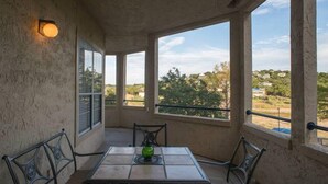 A covered patio with a table and chairs, large windows with a view of greenery and buildings, and a wall-mounted light fixture. - Charming and spacious Villa with a big wrap around Balcony (Lago Vista)