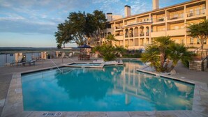 A swimming pool with lounge chairs and umbrellas, a building with balconies, and a view of the water. - Charming and spacious Villa with a big wrap around Balcony (Lago Vista)