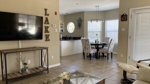 A living room with a TV, a glass coffee table, and a dining area with patterned chairs. - Charming and spacious Villa with a big wrap around Balcony (Lago Vista)
