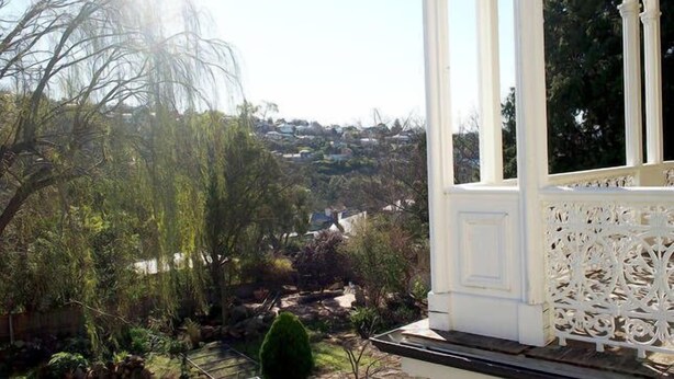 A view from a porch with white columns and intricate railing, overlooking a residential area with trees and houses. - Toogooloowa on Davey 5 (Hobart)