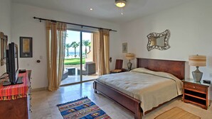 A spacious bedroom with a large bed, a sliding glass door leading to a balcony, a television, and a desk with a computer.