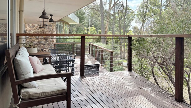 A wooden deck with a stone wall, a bench, and a table with chairs.
