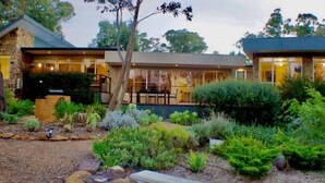 A modern house with a stone exterior, a patio with a bench, and a well-maintained garden with various plants and shrubs.