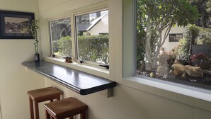 Une cuisine dotée d’un plan de travail noir, de deux tabourets en bois et d’une fenêtre donnant sur un jardin.