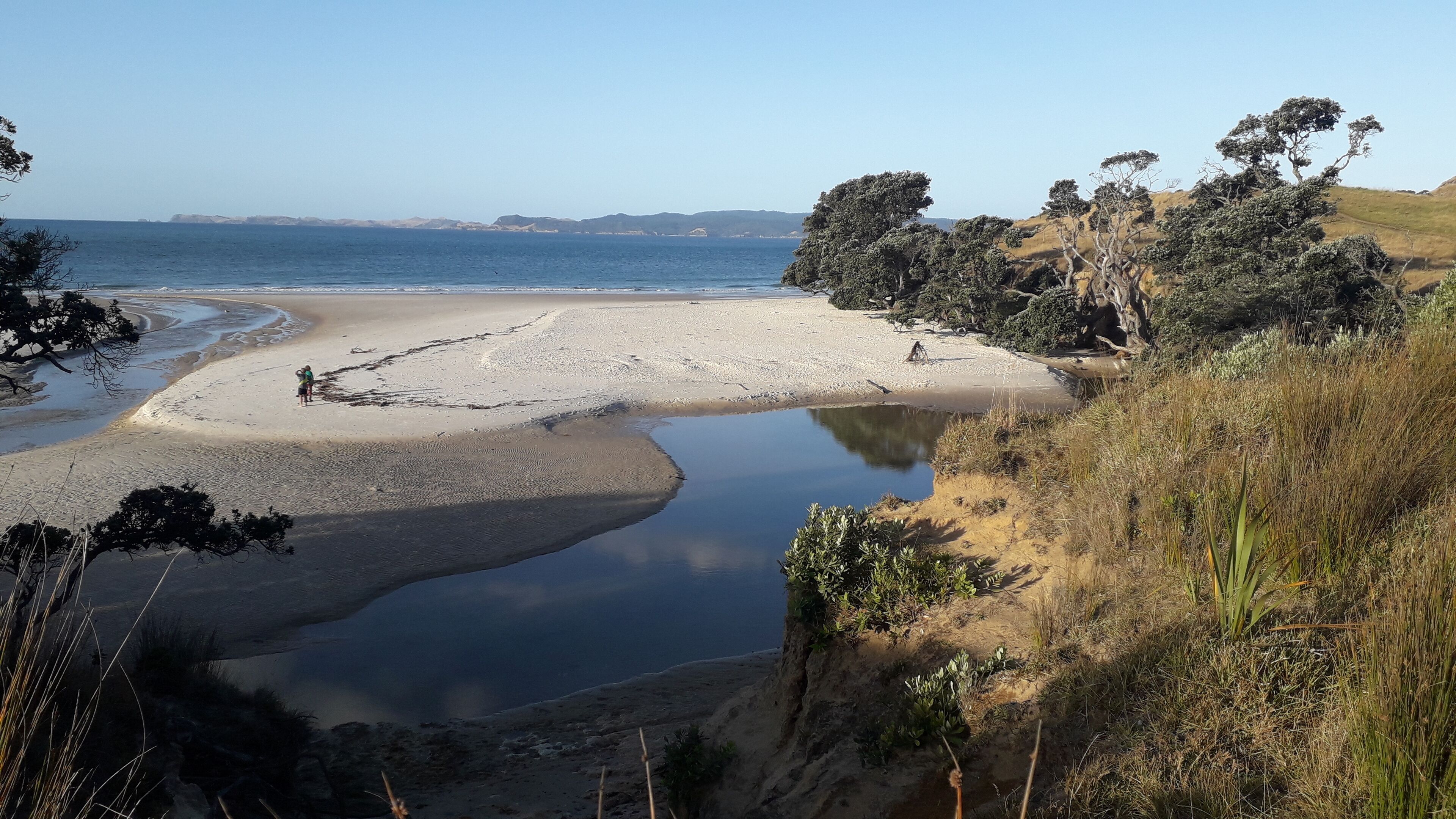 Un paysage côtier comprenant une plage de sable, un petit plan d’eau et une végétation environnante.