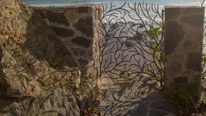 A stone staircase leading to a coastal area with a clear view of the sea and distant hills.