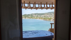 A bedroom with a view of a coastal town and a hot tub.