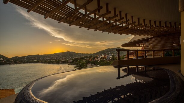 A pool with a view of a sunset over a hilly landscape.