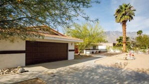 Propiedad residencial con garaje, entrada para vehículos y jardín ajardinado con palmera y plantas típicas del desierto.