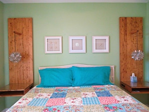 A bedroom with a bed, a teal pillow, a quilt, and three framed pictures on the wall. - The Inn at Dauphin Island Unit 103 (Dauphin Island)