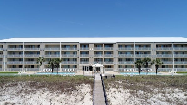Un hotel de varios pisos con zona de piscina, una galería techada y una playa de arena frente a él.