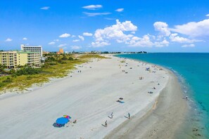 Uma praia com céu claro, areal arenoso e edifícios ao fundo.