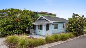 A small, single-story house with a light blue exterior, a porch, and a small garden area with various plants.