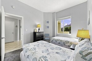 Une chambre avec deux lits, une commode, une chaise, une fenêtre donnant sur un paysage agréable et une porte.