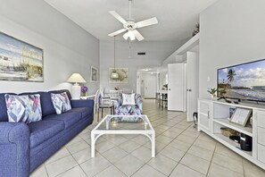 A modern living room with a blue sofa, a coffee table, a ceiling fan, and a television on a stand.