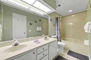 Une salle de bain avec un grand miroir, deux lavabos, des toilettes et un espace douche.