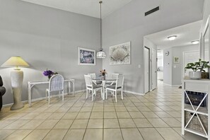 Un intérieur moderne avec un coin repas comprenant une table ronde et des chaises blanches, une lampe et des œuvres d’art accrochées aux murs.