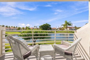 A balcony with wicker furniture overlooking a lake and a golf course. - Isla Del Sol 2BR Corner Condo w/ Golf Views (Isla Del Sol)