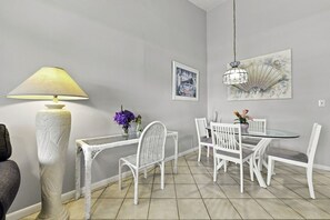 Ein Essbereich mit einem runden Tisch, weißen Stühlen, einer hohen Stehlampe und einer Pendelleuchte.
