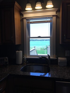 Enjoy a kitchen with a view of the water through a large window, featuring a granite countertop, stainless steel sink, and wooden cabinets.