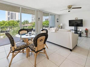 A modern living room with a sofa, television, and dining area with chairs. - 1BR Marco Island condo with heated pool, WiFi, and full kitchen. (Marco Island)