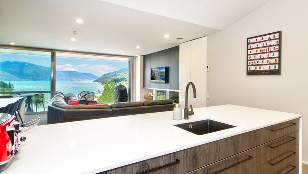 A modern kitchen with a large island, a built-in dishwasher, and a view of a lake and mountains.