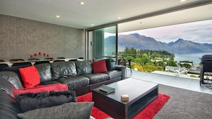 A modern living room with a leather sofa, a coffee table, and a view of mountains and a lake.