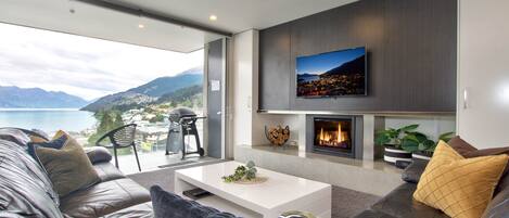 A modern living room with a fireplace, a flat-screen TV mounted on the wall, and a sofa with cushions.