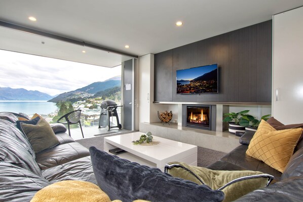 A modern living room with a fireplace, a flat-screen TV mounted on the wall, and a sofa with cushions.