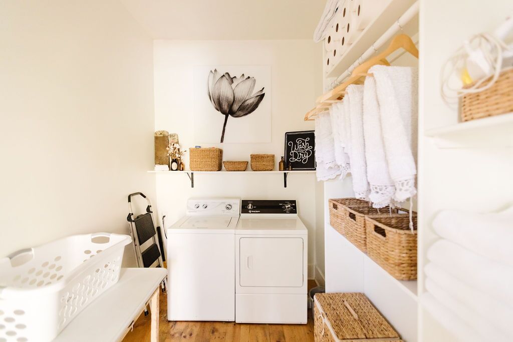 A laundry room with a washing machine, drying rack, baskets, and a wall-mounted flower decoration.