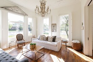 A bright, open living room with a white sofa, a wooden coffee table, and a chandelier. - Historical Morrow House Season 5 Fixer Upper, Featured In Cottage Style Magazine (Waco)