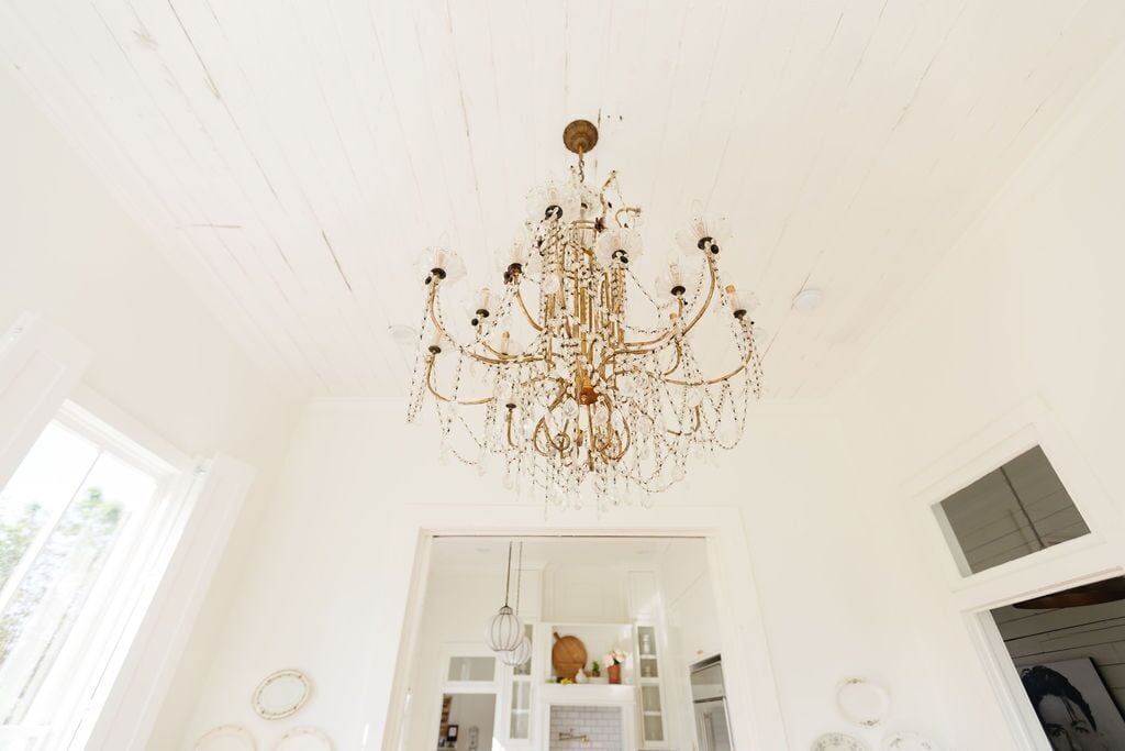 A chandelier in a bright room with white walls and a visible doorway leading to another room.