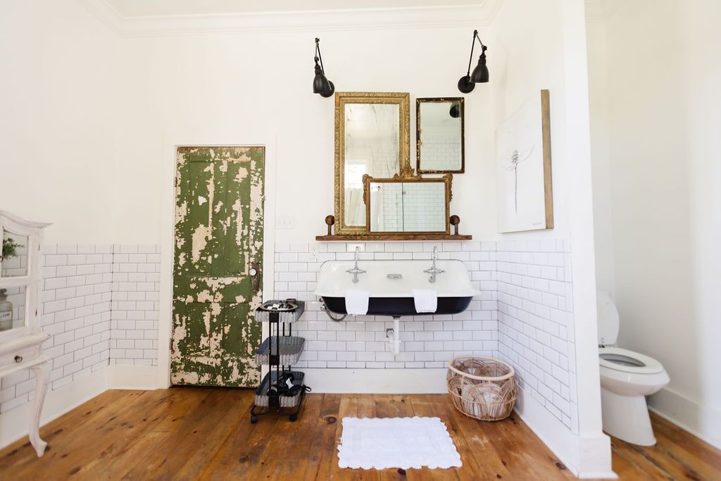 A bathroom with a white tiled wall, two sinks, a mirror, and a wooden floor.