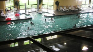 Une piscine intérieure dotée de plusieurs couloirs de nage, de chaises longues et offrant une vue sur l’extérieur grâce à de grandes fenêtres.