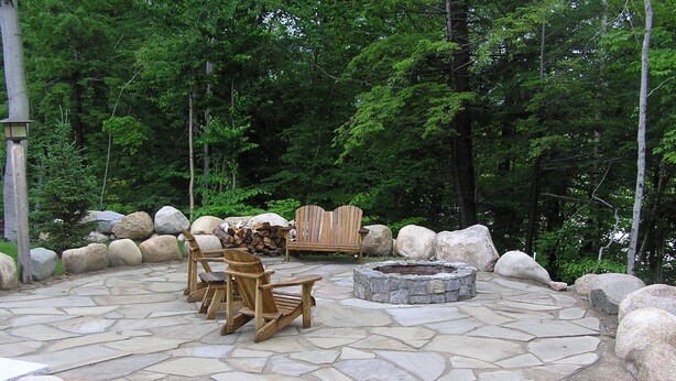 Une terrasse en pierre avec des fauteuils Adirondack, un foyer et un fauteuil Adirondack en bois.