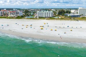 A beach with umbrellas and people, a coastline, and buildings in the background. - Sunset Vistas 610N: Top Floor Gulf Front Beauty (Treasure Island)