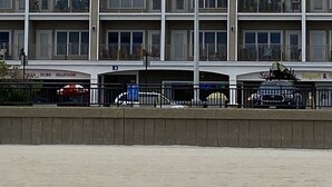 Et hotel med flere etager og et tydeligt skilt med 'Sea Spray'. Der er altaner på hver etage, og en indgang i stueplan med et skilt for 'Pizza - Subs - Seafood'.