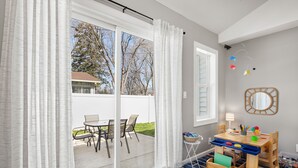 Ein Zimmer mit einer Glastür, die auf eine Terrassengrundstück führt, einem Holztisch mit Stühlen, einem kleinen Beistelltisch und einem Spiegel an der Wand.