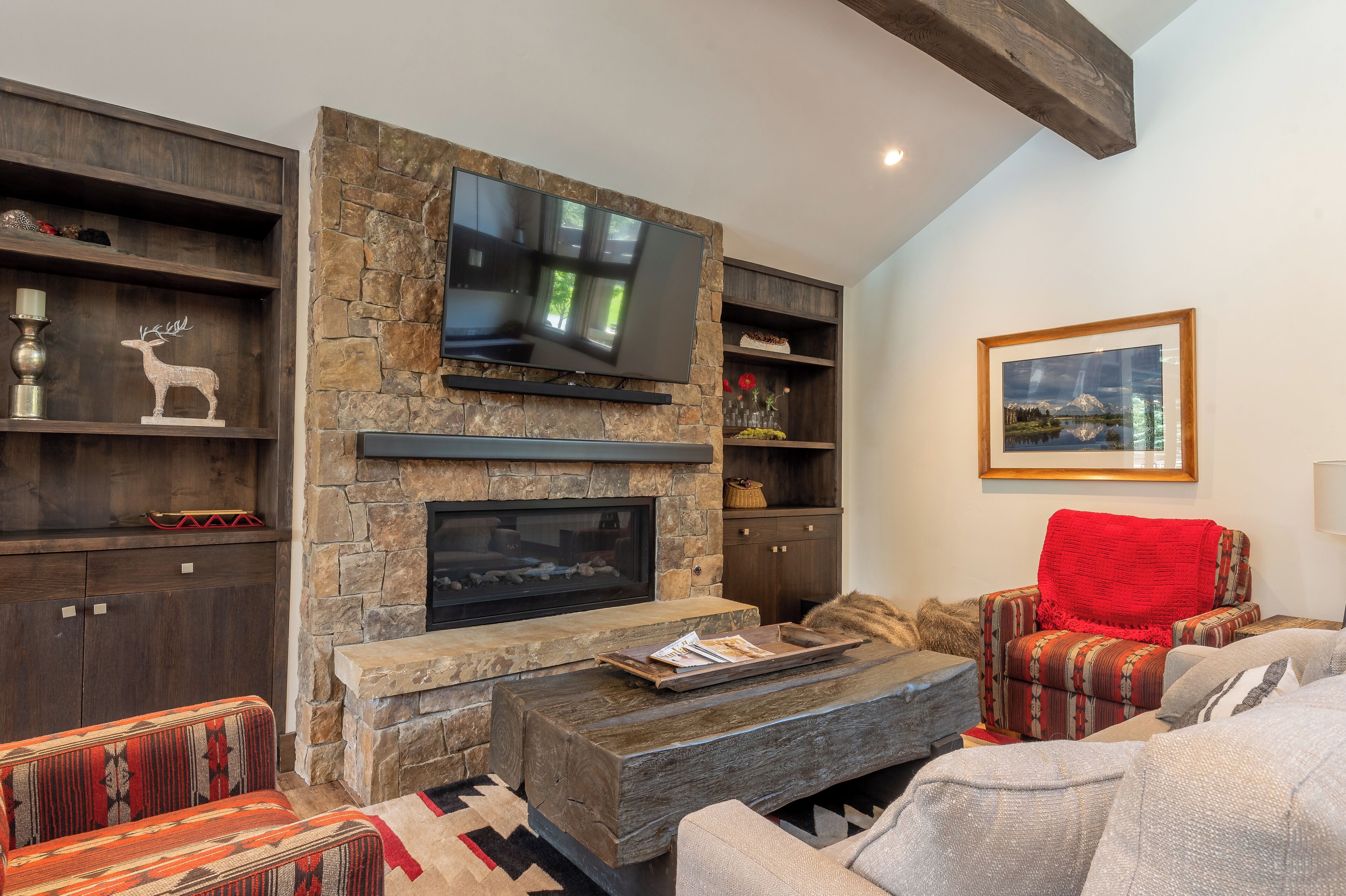 A modern living room with a stone fireplace, a flat-screen TV, and a cozy seating area with patterned cushions.