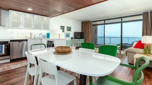 A modern kitchen with white cabinets, stainless steel appliances, and a dining area with a white table and green chairs. - Adorable one bedroom oceanfront with a pool (Ocean City)
