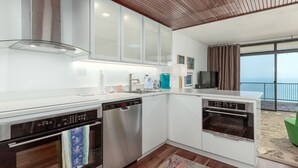 A modern kitchen with white cabinets, stainless steel appliances, and a wooden ceiling. - Adorable one bedroom oceanfront with a pool (Ocean City)