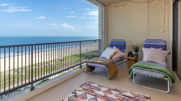 A balcony with a view of the beach, two lounge chairs, a patterned rug, and string lights. - Adorable one bedroom oceanfront with a pool (Ocean City)
