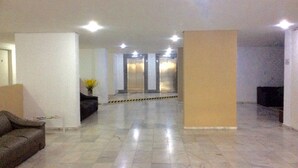 Un hall d’entrée spacieux avec un sol en marbre, un comptoir d’accueil, un canapé et un ascenseur.