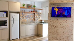 Une cuisine moderne équipée d’un four à micro-ondes, d’un réfrigérateur, d’un four et d’un évier. Le mur derrière le plan de travail est recouvert de carreaux, et un autre mur présente un motif en briques. Un téléviseur est fixé au mur.